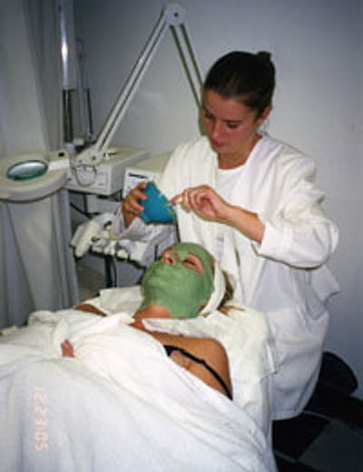 An esthetics student applying a facial mask to a client in the school facial room